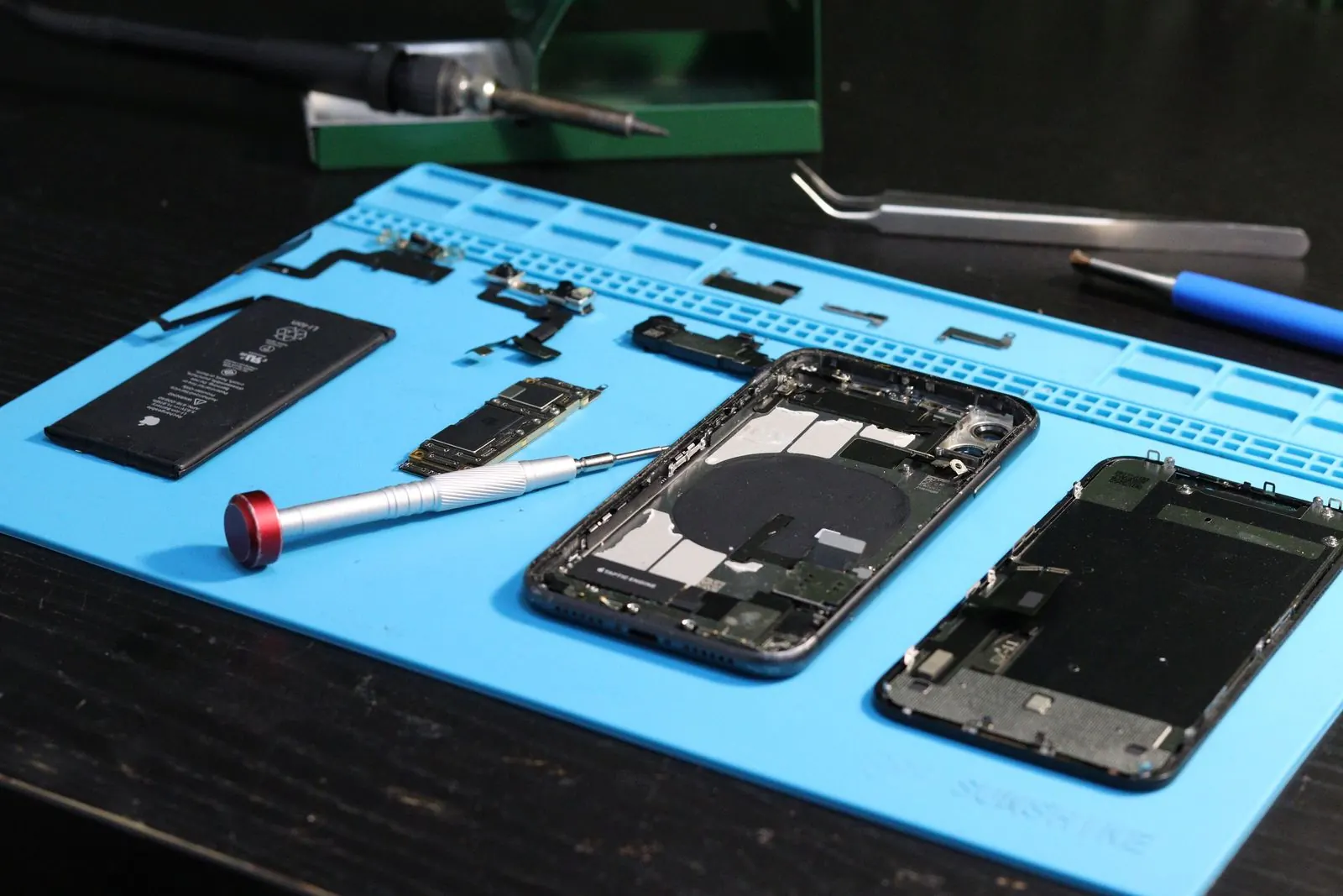 iPhone démonté sur un tapis d’atelier, pièces rangées autour